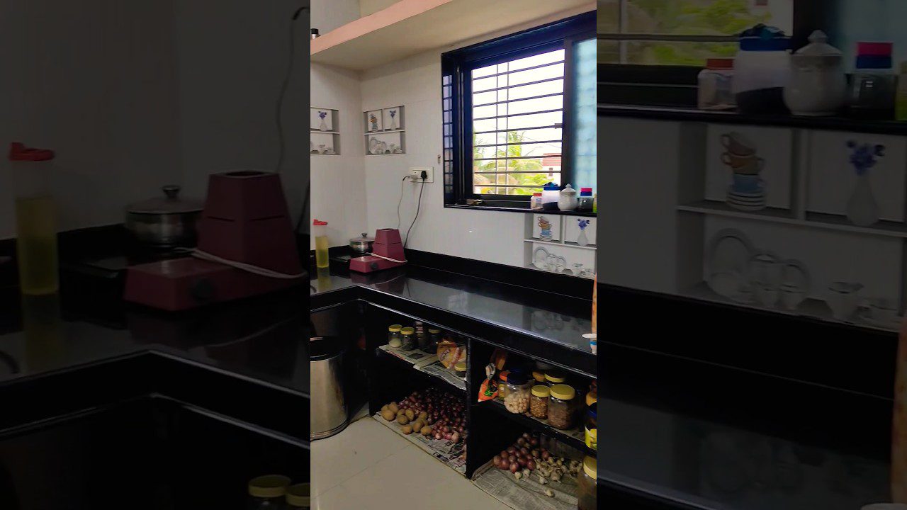 Virtuvės kampas su juodu stalviršiu, indais, prieskoniais ir daržovėmis po lentynomis