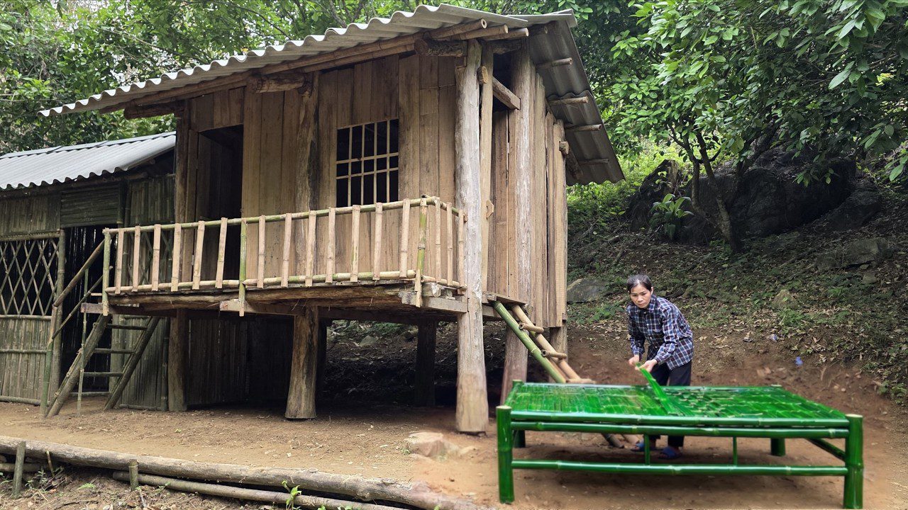 Senovinė trobelė ant stilčių miške ir moteris, pinti bambukinį čiužinį