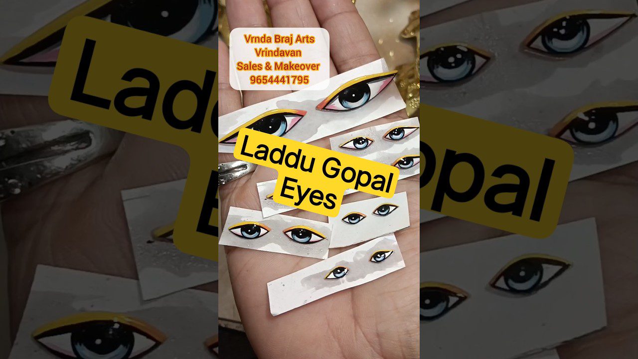 Rankoje laikomi keli dekoratyvūs iškirpti akies piešiniai su geltonu akių kontūru ir tekstu „Laddu Gopal Eyes“.