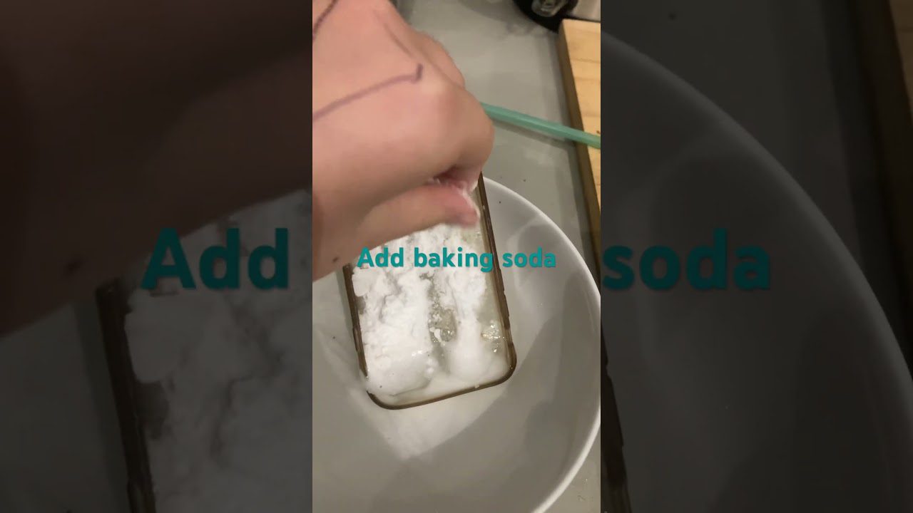 Rankos barsto kepimo sodą ant telefoną dengiančio stiklo, tekstas „Add baking soda“ įrašytas.