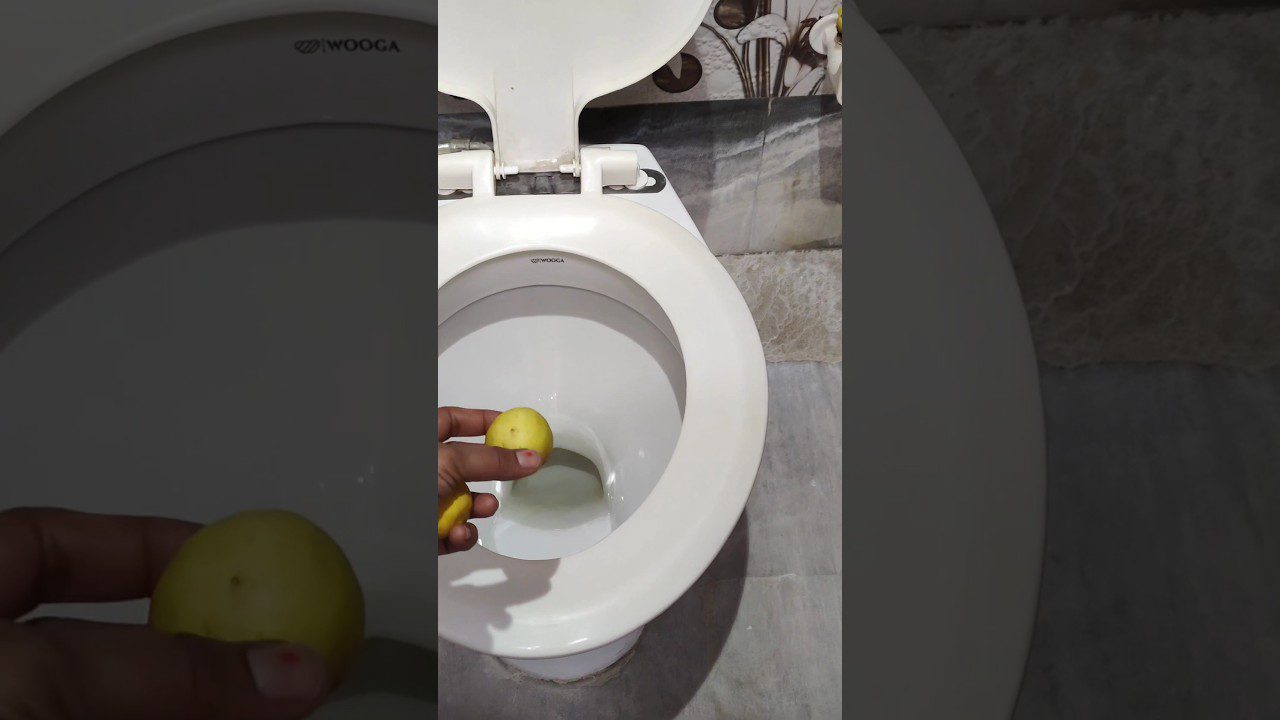 Rankoje laikomas geltonas obuolys virš atviro tualeto dubens vonios kambaryje