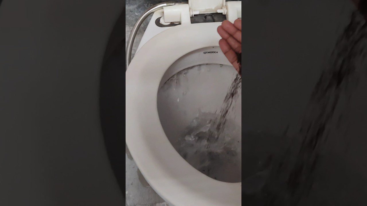 Rankos pilant vandens iš žarnos į tualeto dubenį, vanduo teka ir putoja.