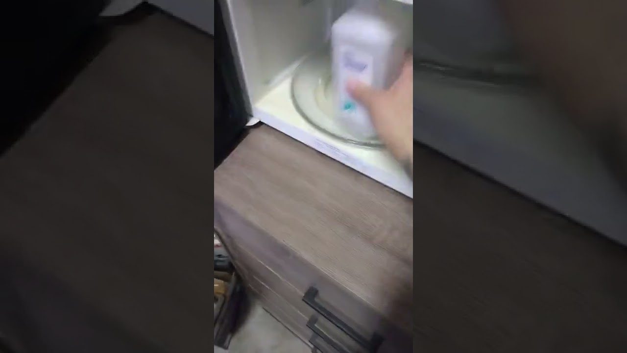 Rankomis dedama dezodoranto tūtelė ant besisukančio mikrobangų krosnelės lėkštės.