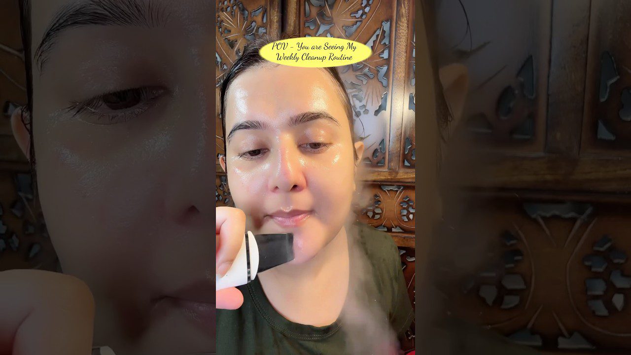 Moteris naudoja veido garinimo aparatą prie skruosto, blizganti oda, tekstas viršuje: "POV – You are Seeing My Weekly Cleanup Routine"