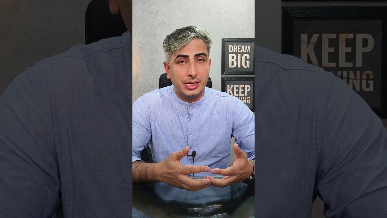 Vyriškis su pilkais plaukais kalba priešais mikrofoną, fone užrašai „Dream Big“ ir „Keep Going“