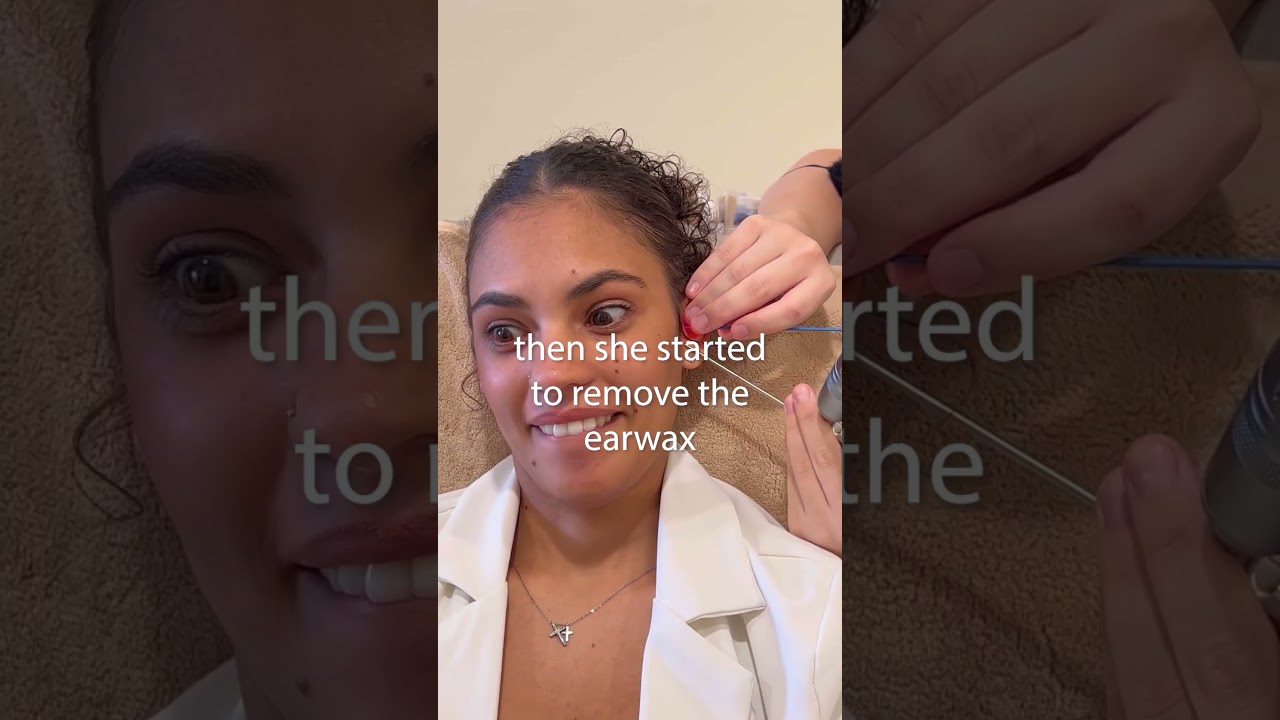 Moteris gulėdama šypsosi, ausyje specialiu įrankiu šalinamas ausų vaškas, užrašas „then she started to remove the earwax“