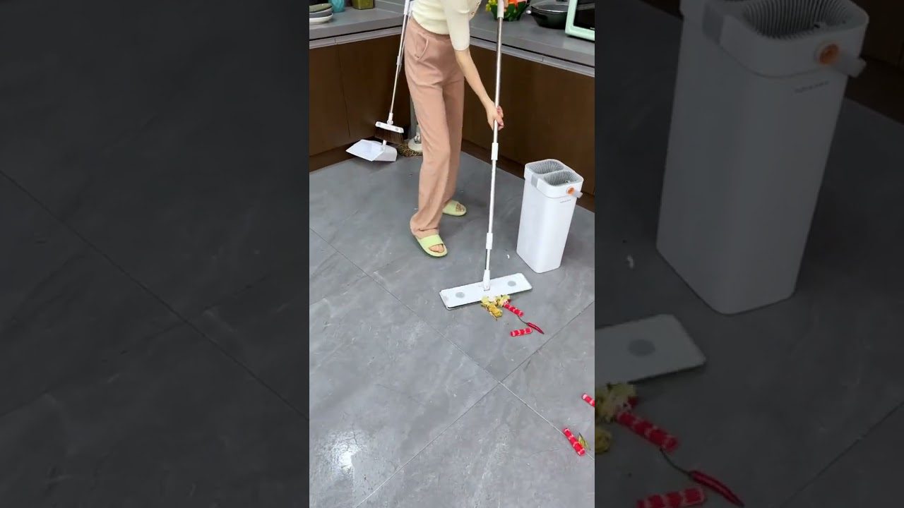 Moteris grindis valo plytelių virtuvėje su balta plokščia šluota ir kibiru.