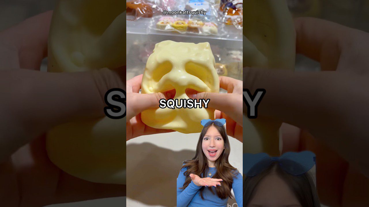 Rankose spaudžiamas geltonas katės formos squishy žaislas su angomis akims ir burnai