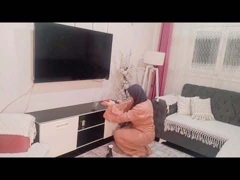 Moteris su galvos apdaru tvarko spintelę po pakabintu televizoriumi svetainėje, šalia sofa.