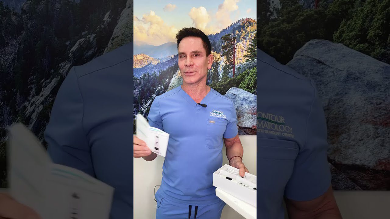 Dermatologas mėlynais chalatais laiko odos priežiūros rinkinį prieš kalnų peizažą.