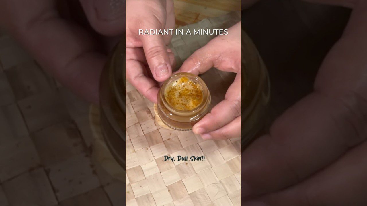 Rankose laikomas atidarytas kosmetikos indelis su geliniu, aukso spalvos šveitikliu ir užrašu "Radiant in a minutes".