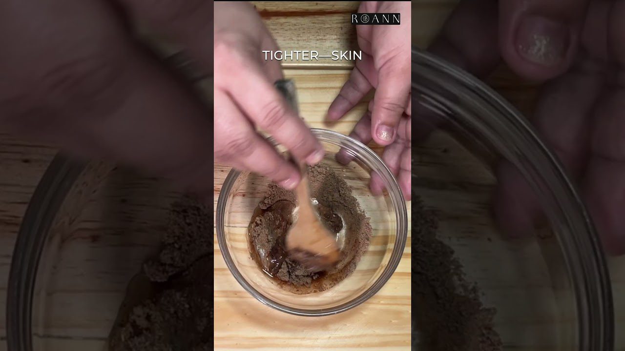 Rankos maišo kavamą ir medų į stiklinį dubenėlį ant medinio stalo, užraše „Tighter—Skin“.