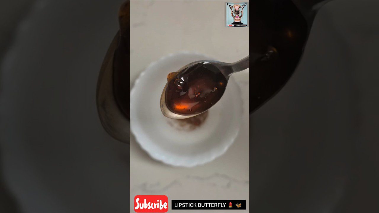 Šaukštas su tamsiu medumi virš mažos baltos lėkštelės, apačioje užrašas „Subscribe“ ir „LIPSTICK BUTTERFLY“