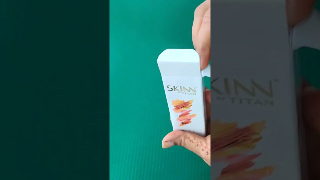 Rankoje laikoma baltos pakuotės kosmetinė dėžutė su užrašu SKINN ir dažų ženklais
