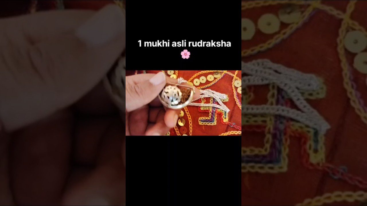 Rankoje laikomas sidabrinis žiedas su baltu rudrakša karoliuku ant raudono siuvinėto fono