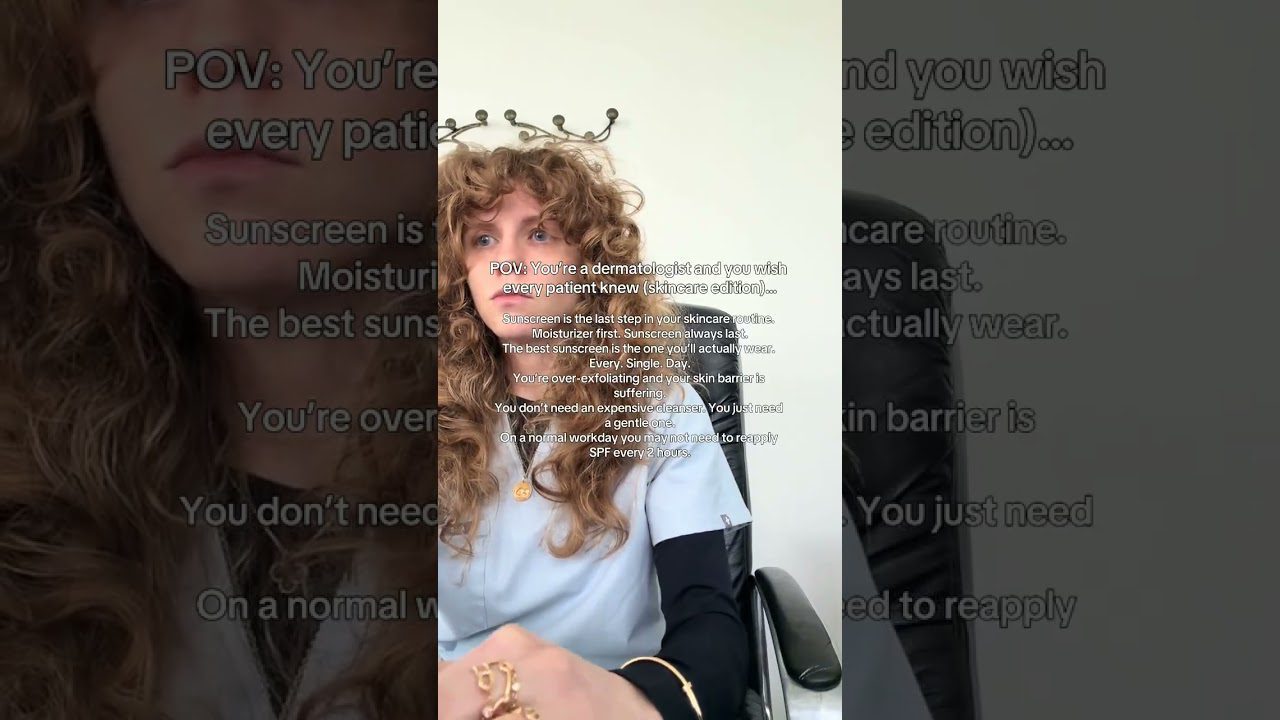 Dermatologė su garbanotais plaukais apsirengusi darbo drabužiais sėdi kėdėje ir kalba apie odos priežiūrą.