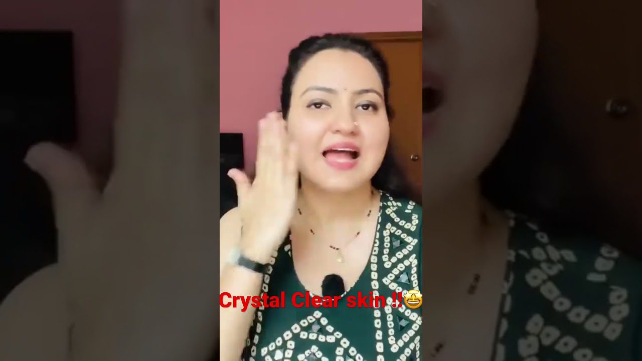 Moteris rodo veidą ir braukia ranka per skruostą, užraše „Crystal Clear skin“.