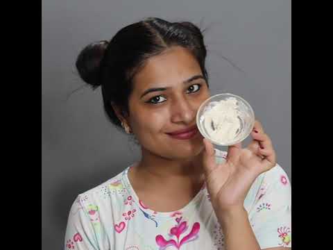 Jauna moteris su kuodeliais laiko indelį su kremu ir šypsosi žiūrėdama į kamerą