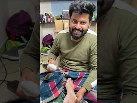 Vyras šypsosi skustuvu glostydamas kito koją, aplink matyti daiktai ir dėžės