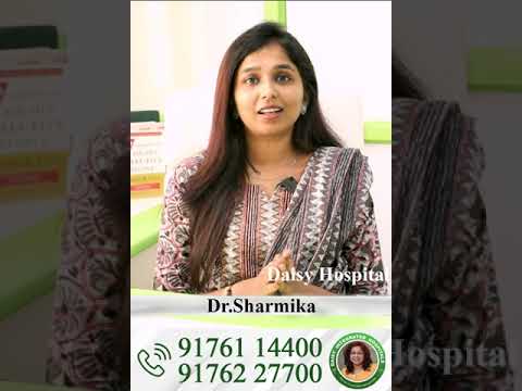 Jauna gydytoja Sharmika sėdi kabinete, šypsosi, matomi kontaktų numeriai ir ligoninės logotipas