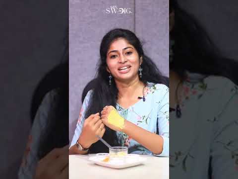 Jauna moteris sėdi prie stalo, šypsosi ir ragauja desertą šaukštu.