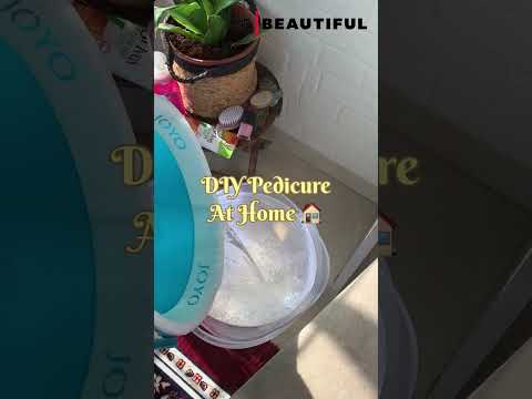 Vonelė kojų prie augalo ir kosmetikos, užrašu "DIY Pedicure At Home" viršuje.