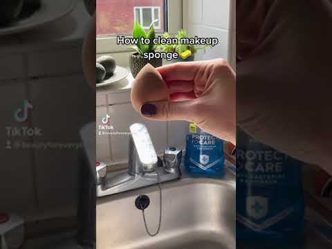 Rankoje laikomas rožinis makiažo kempinėlės trintukas virš kriauklės su muilu ir čiaupu