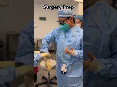 Medikas su apsaugine kauke ir chalatu rengia sterilią pirštinę prieš operaciją.