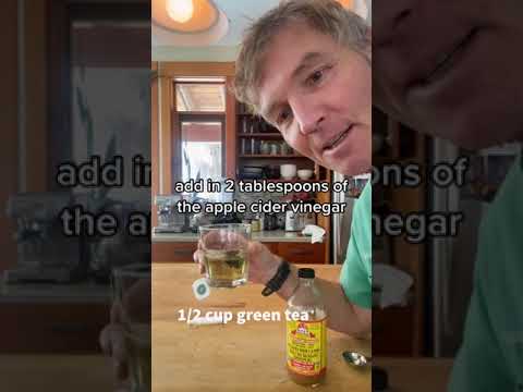 Vyras virtuvėje laiko stiklinę su žalia arbata ir obuolių acto butelis ant stalo, užrašas: „add in 2 tablespoons of the apple cider vinegar“